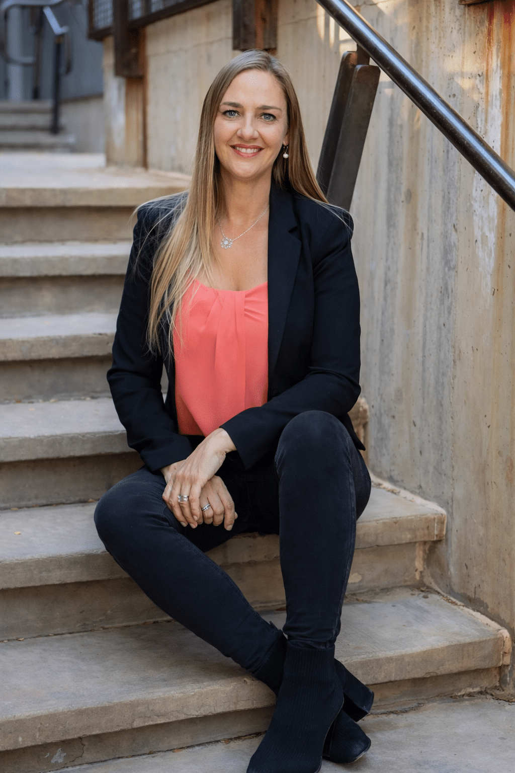 Amy Koch, Desert Ridge real estate agent, sitting on stairs in a professional outfit and smiling at the camera